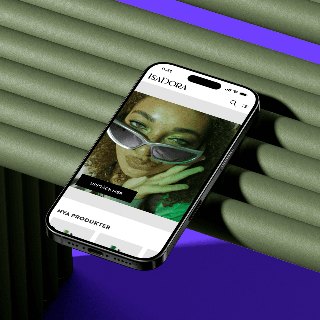 A smartphone displaying IsaDora's website featuring a woman wearing sunglasses. The phone is positioned diagonally on a ribbed green surface with a purple background.