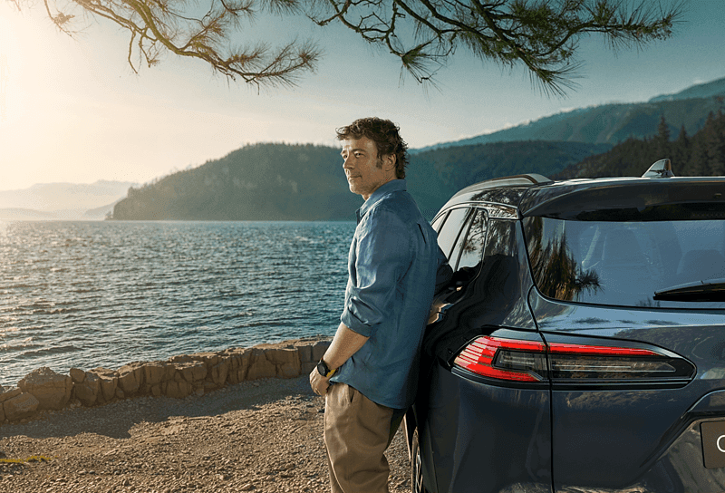 Toyota Center Göteborg Hyrbilar Man leaning against a Toyota car with a view of the sea and mountains.